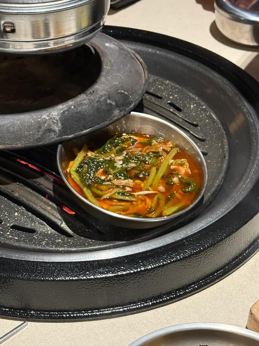 Doenjang jjigae dijaga tetap hangat di kompor samping pada meja BBQ Korea