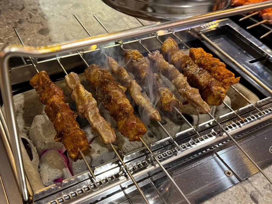 Brochetas de cordero gruesas cocinándose con brochetas más finas para girar de forma uniforme